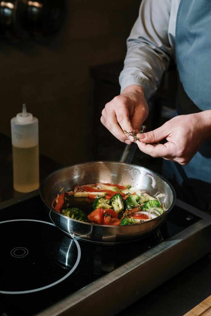 pexels-photo-4252140-4252140 A chef seasons vegetables in a frying pan on a modern stovetop indoors.